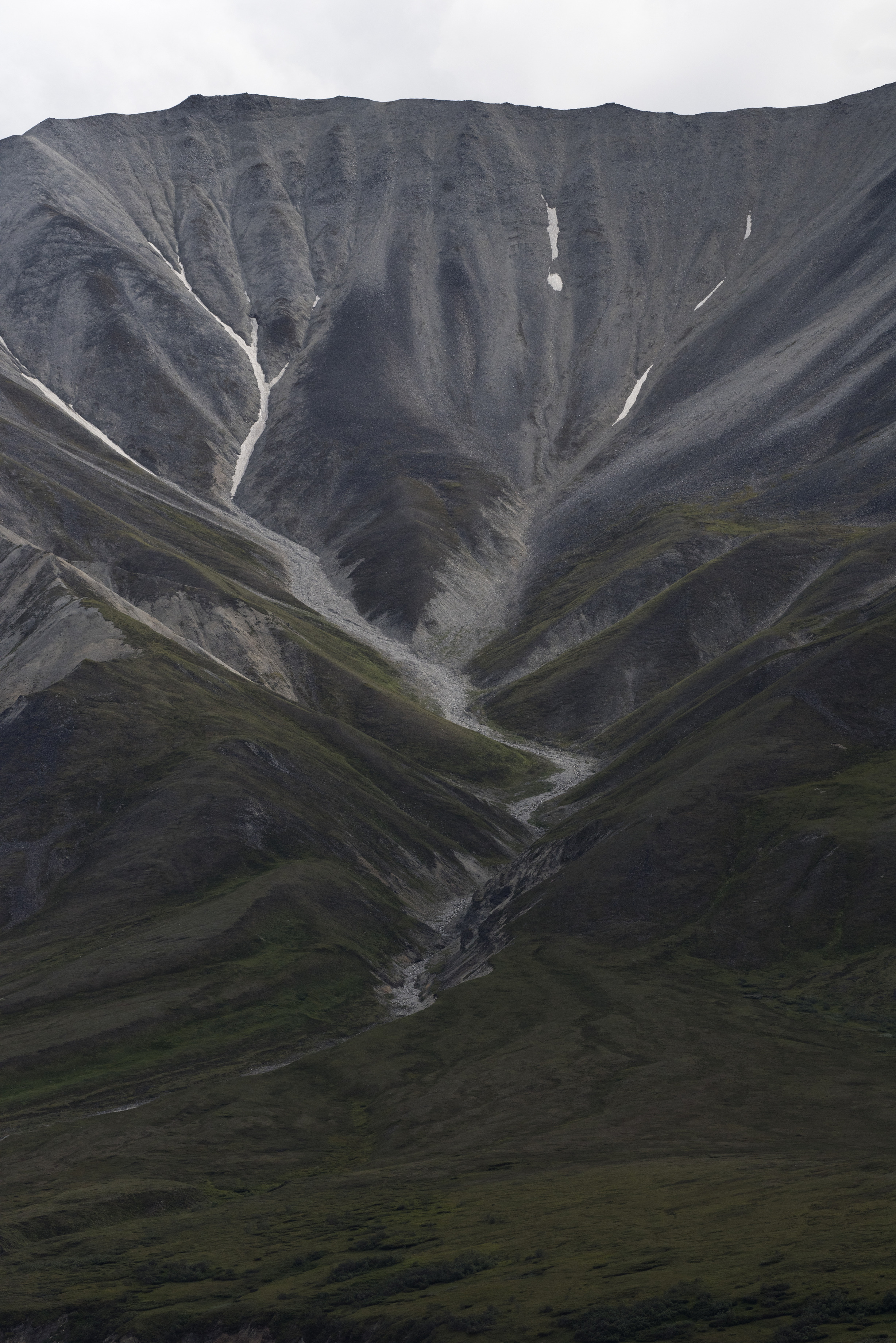 large gray mountain with furrows of snow and water