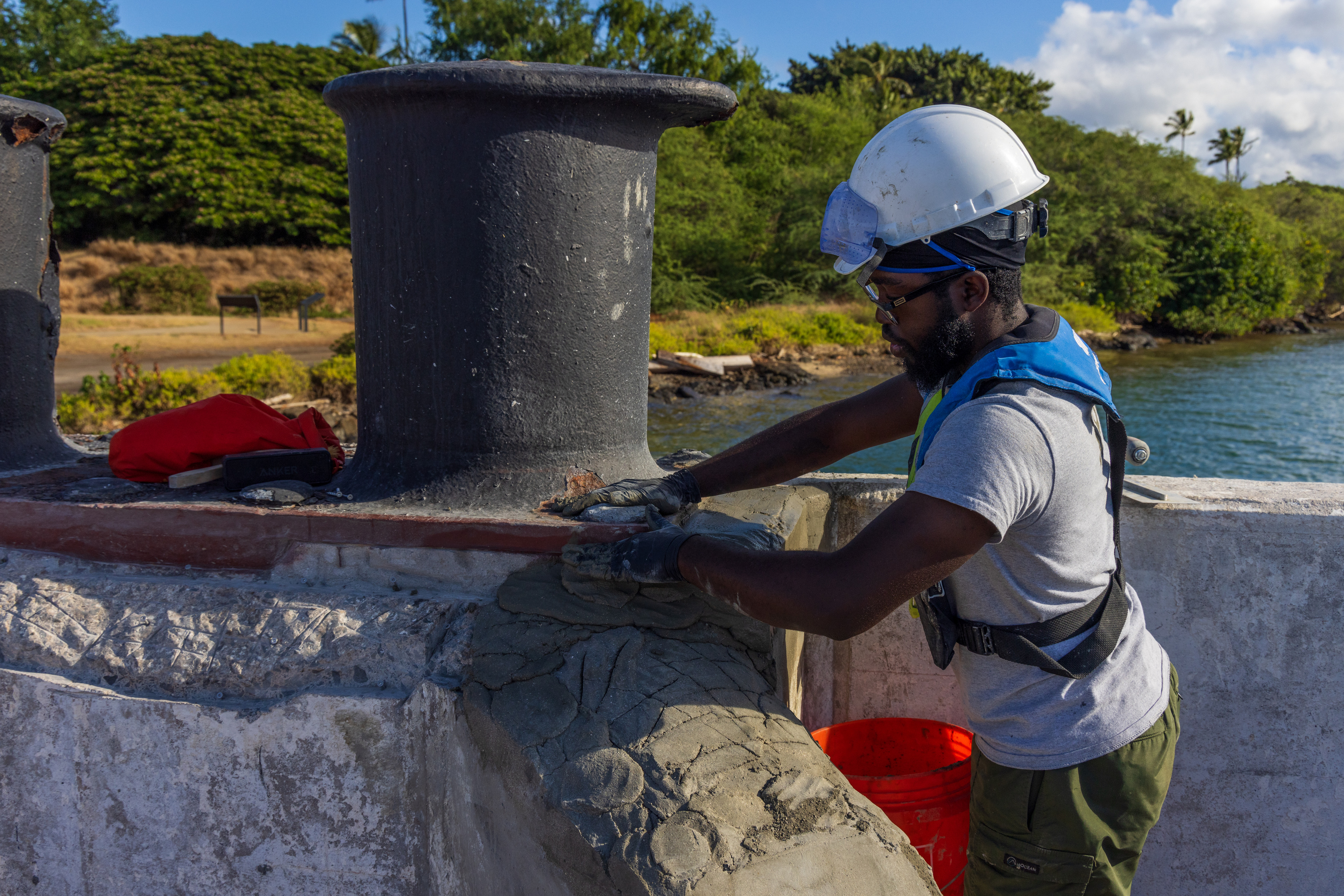 Man in protective gear applies cement to mooring quay by hand, carefully shaping the structure for historical accuracy.