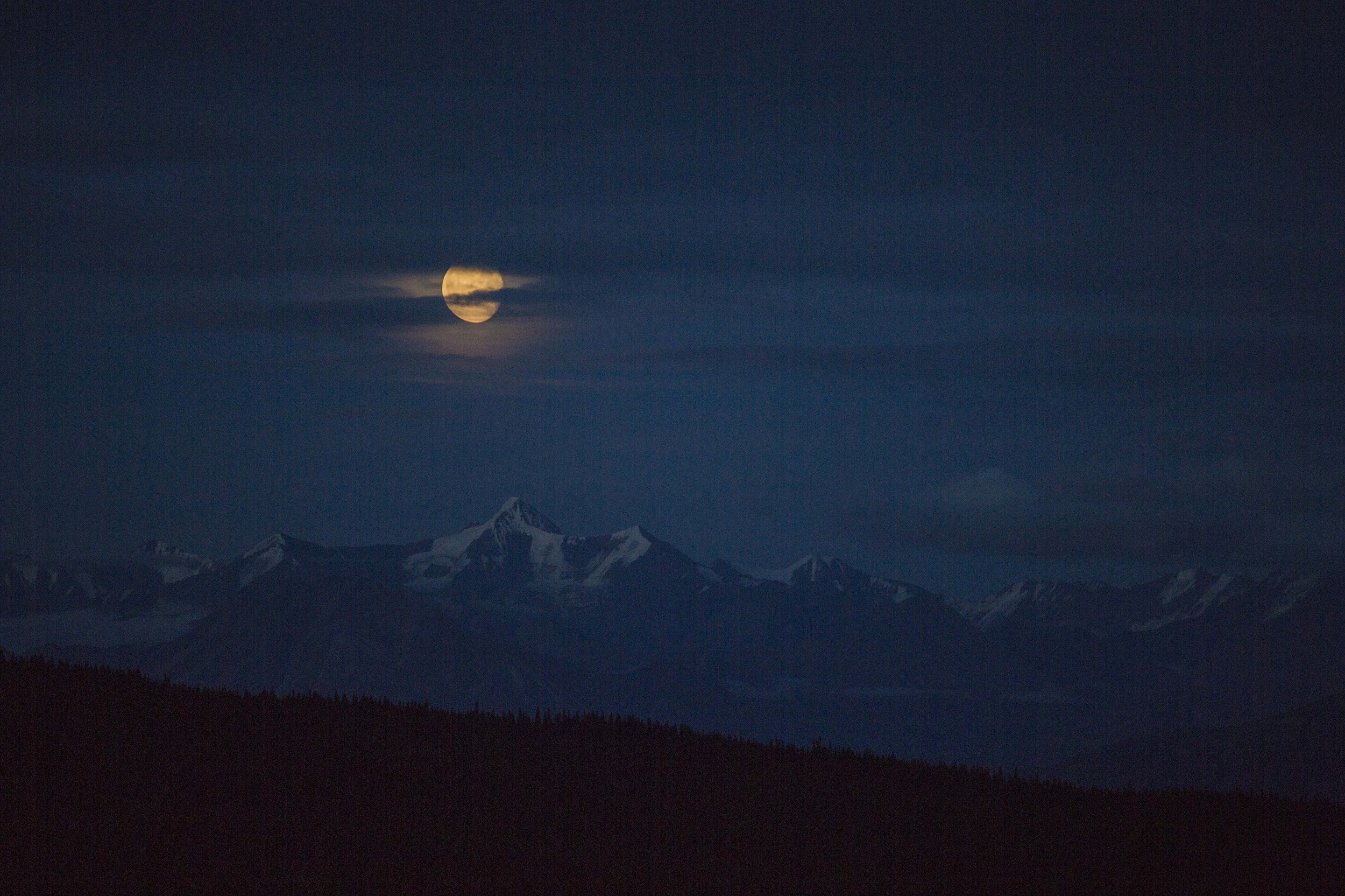 a large pale full moon over snowy mountains