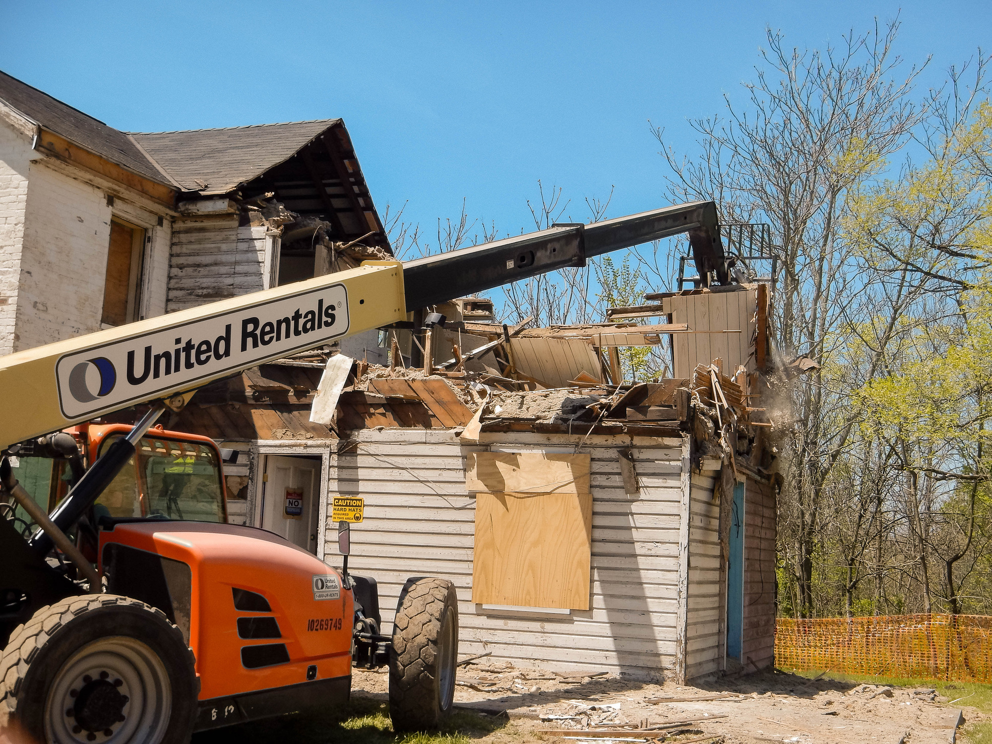 A orange construction machine is shown tearing down the second floor and roof of a white house under construction. 