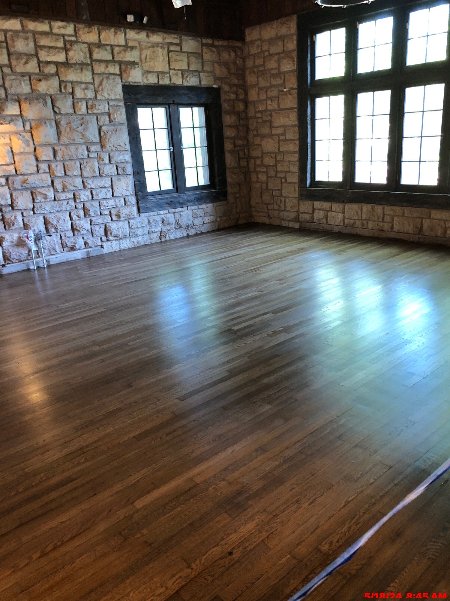 A room in a stone block building with freshly refinished and polished floor, large divided windows in the right wall and a smaller window in the left wall.