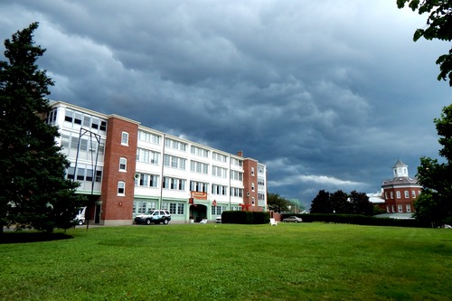 A four-story building with the first floor painted a mint green and the upper floors painted white. Two brick pillars divide the building into three sections.