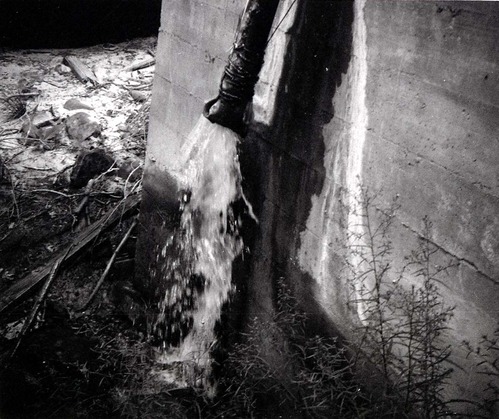 Water pouring on ground from pipe out of cement water tank.
