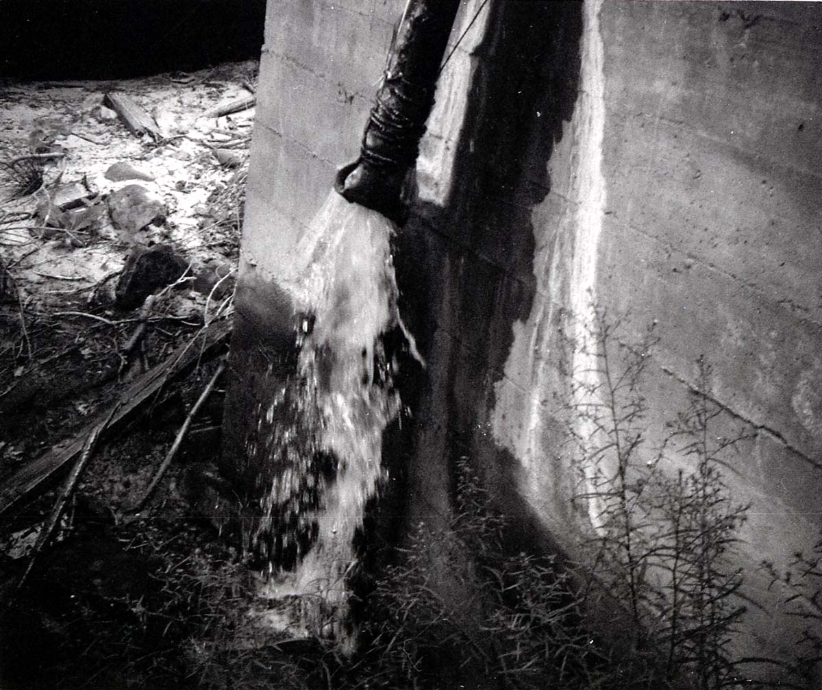 Water pouring on ground from pipe out of cement water tank.
