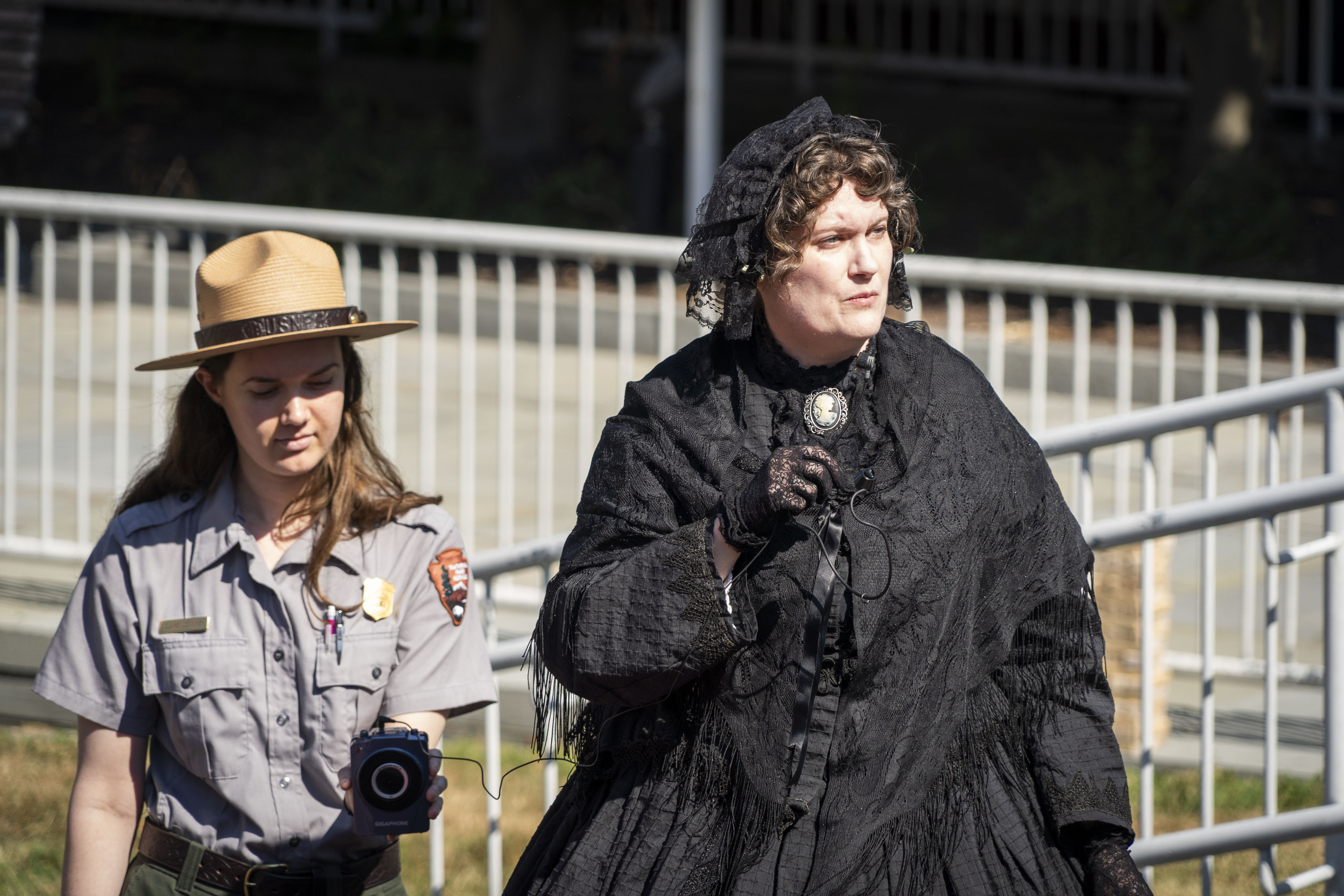 A woman wearing all black speaks into a microphone while a woman in a ranger uniform stands next to her