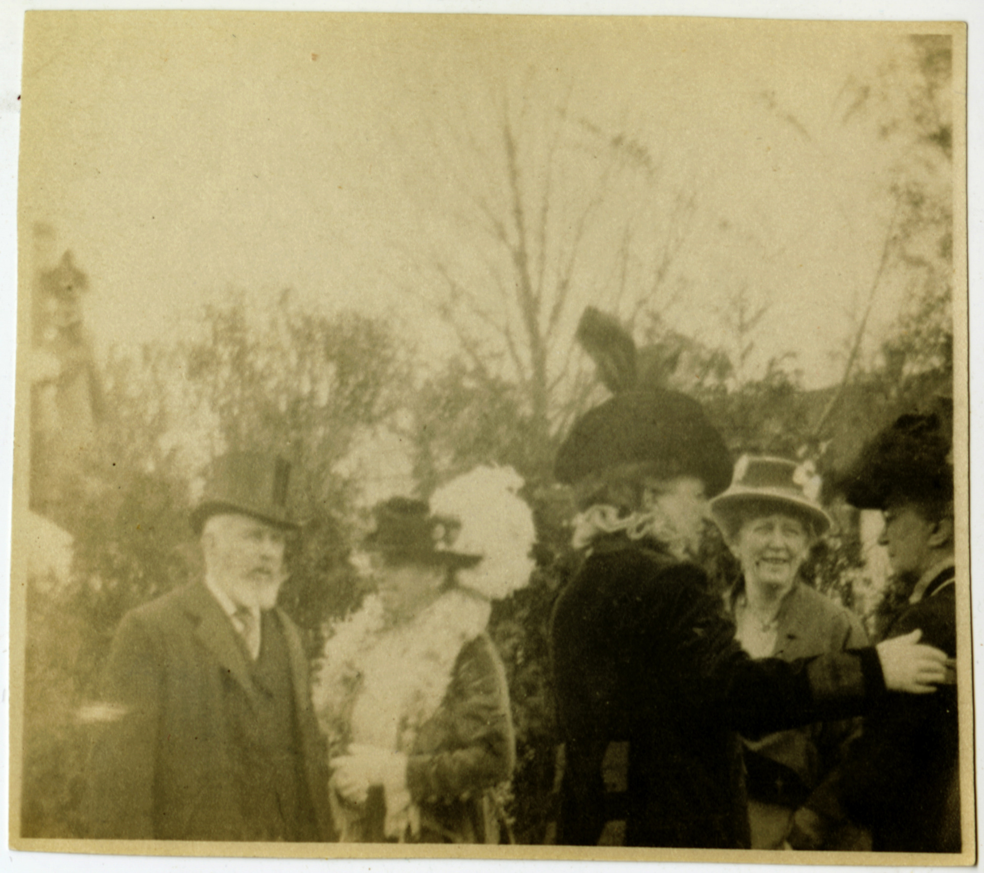 Five white men and women standing outside. They are all wearing dark clothing and hats with some light accents. Trees in background.