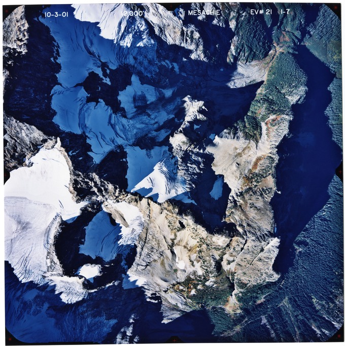 Color aerial photograph of glaciated mountain peak with forested valleys below.