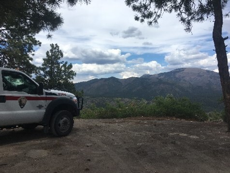 A fire vehicle is parked on the left overlooking a view of mountains and forests