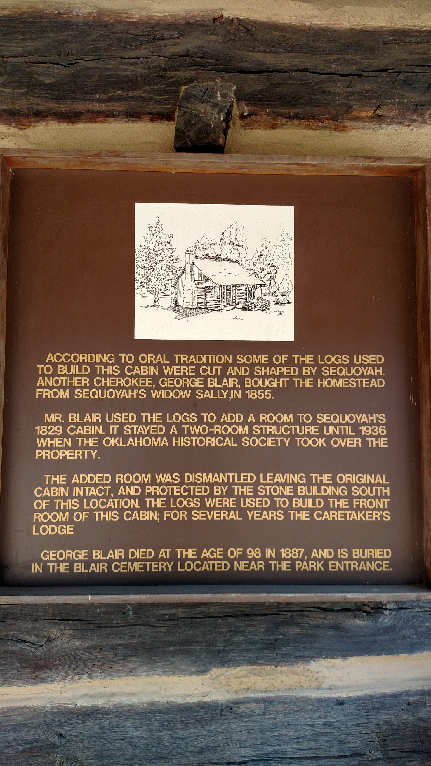A plaque with engraved text and a logo, mounted on a brown background inside a shadowed alcove.