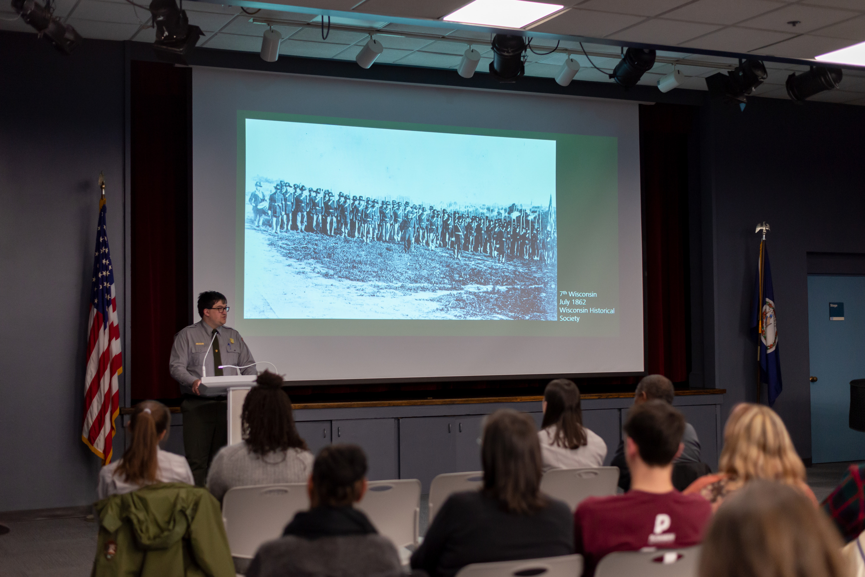 A male park ranger speaks to an audience from a podium.