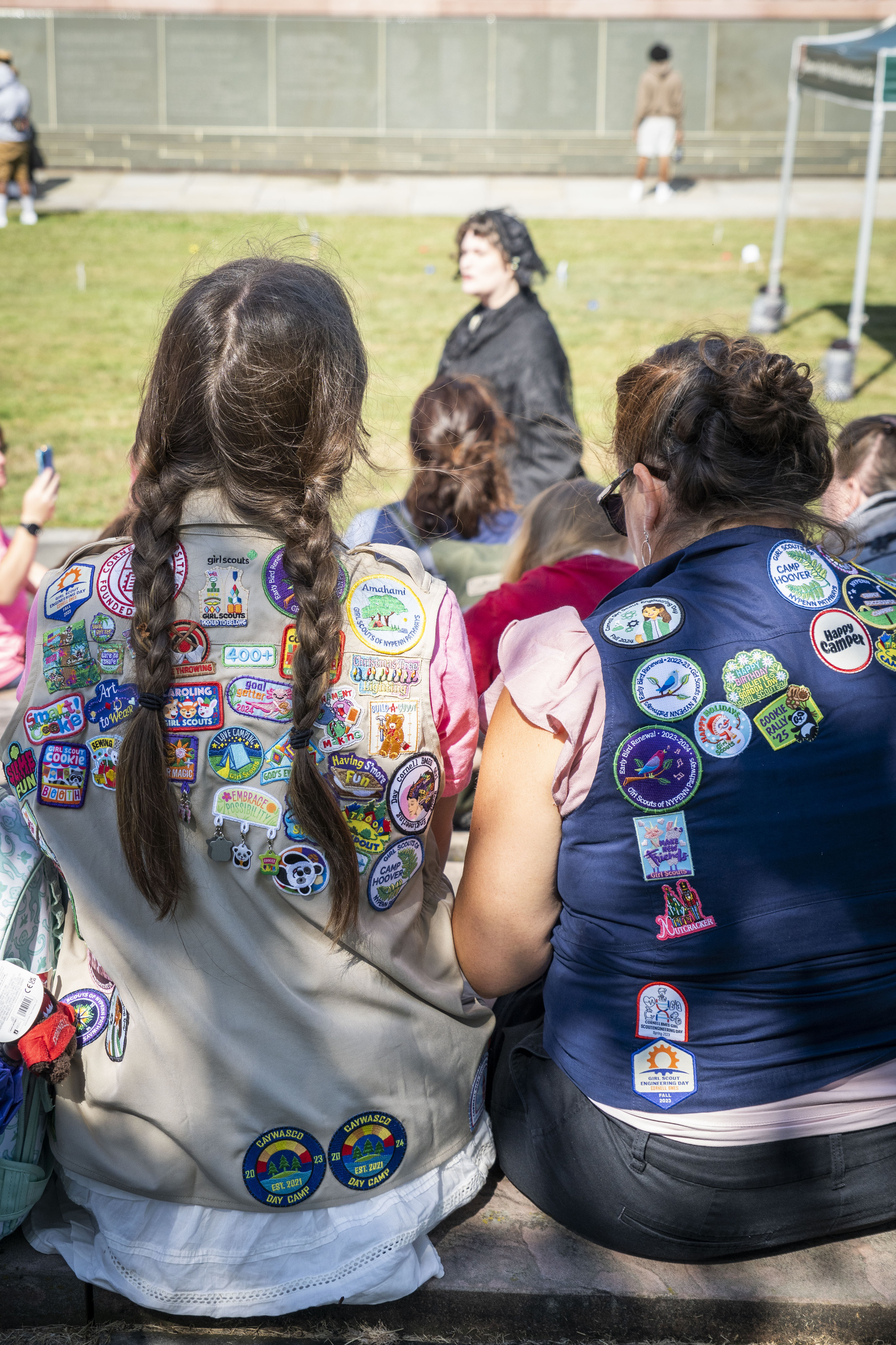 Two girls in vests covered in patches watch a woman speak