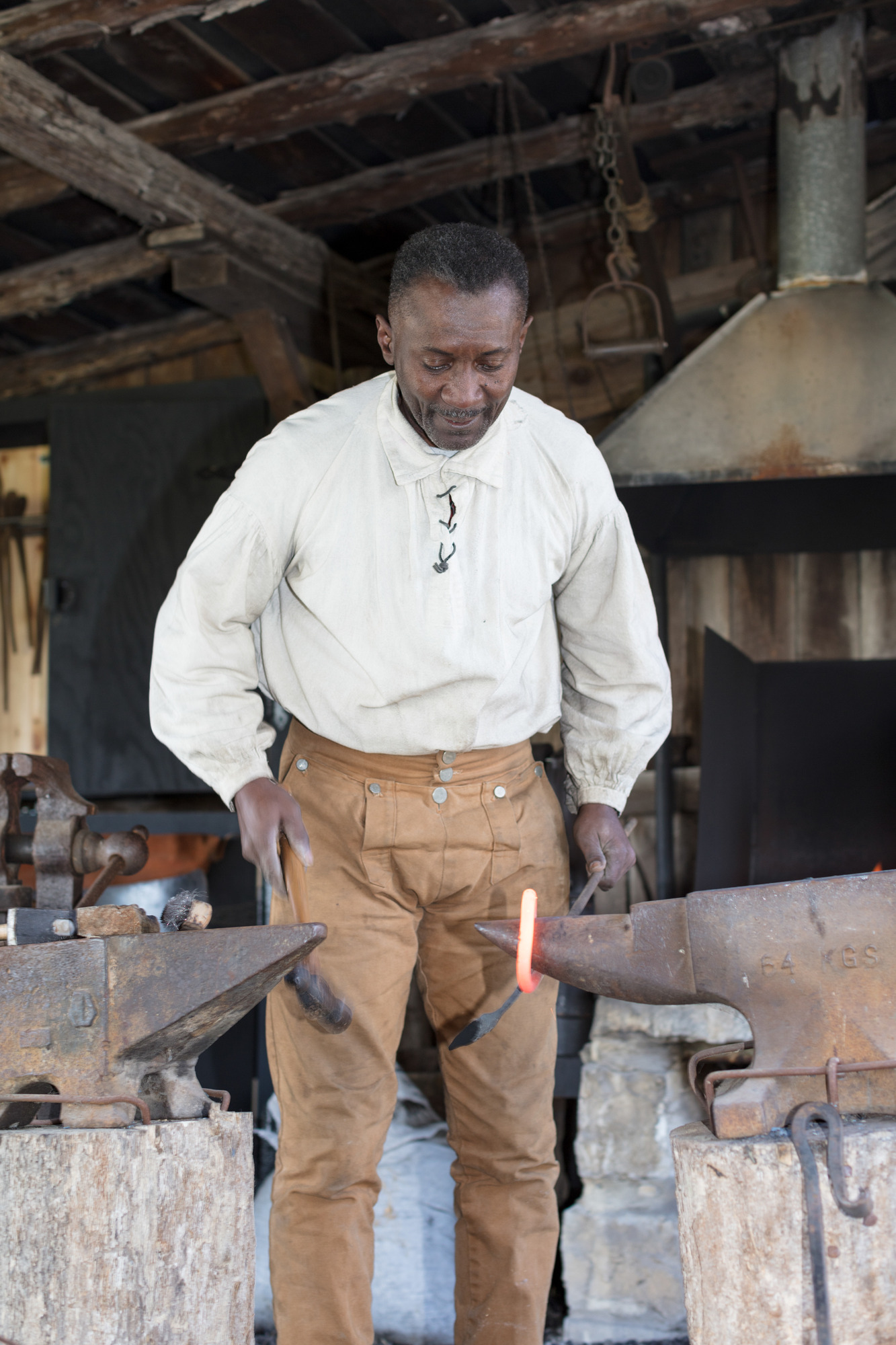 A man in 1800s clothing hammers red hot iron