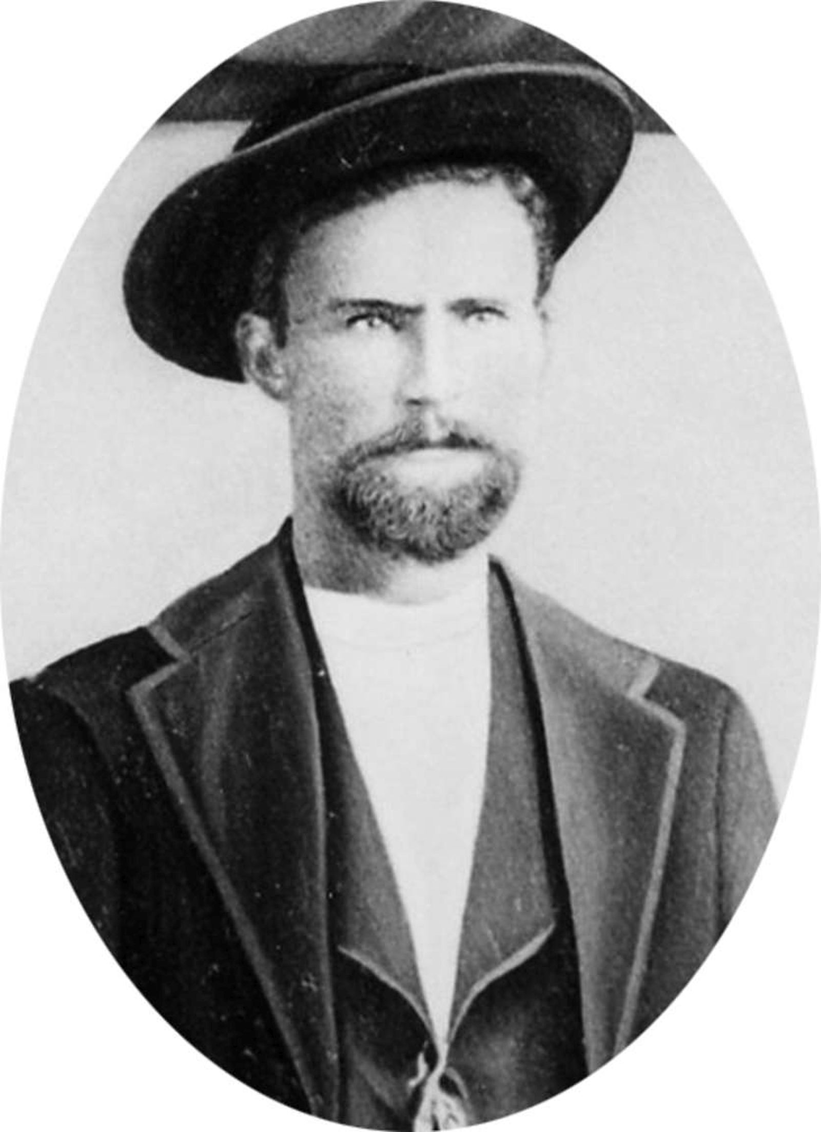 Black-and-white photo of a stern-looking, bearded man wearing a hat, vest, and coat.