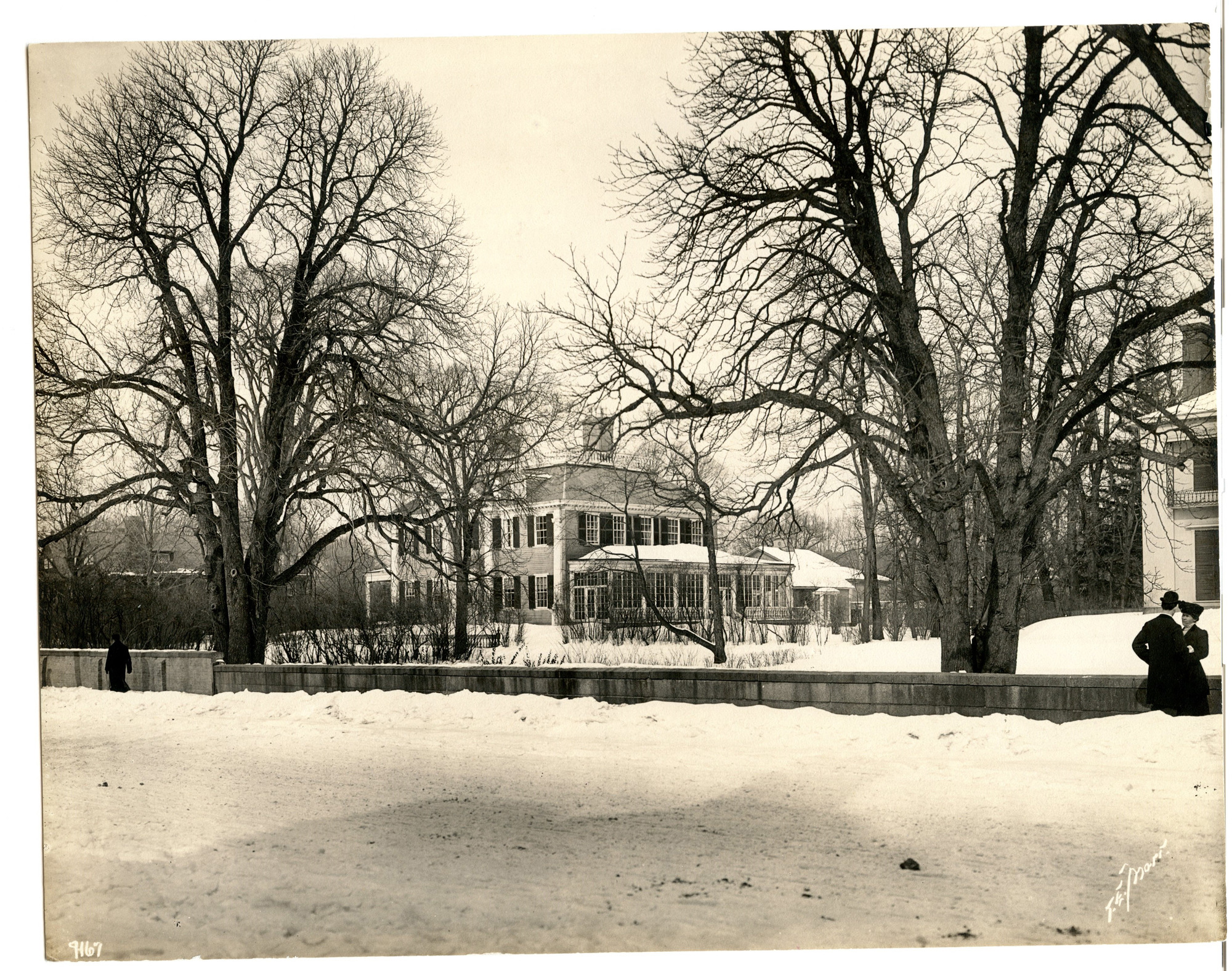 Several people pass through snowy side walks in front of Georgian mansion.