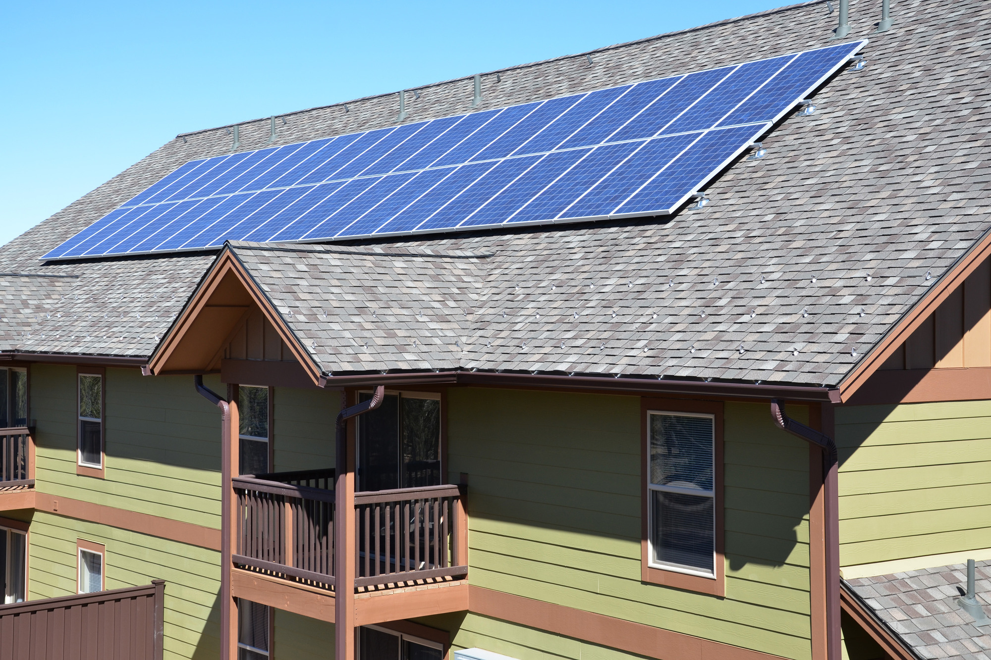 Rectangular grid of a few dozen blue-colored solar panels is perched on a sloped gray roof