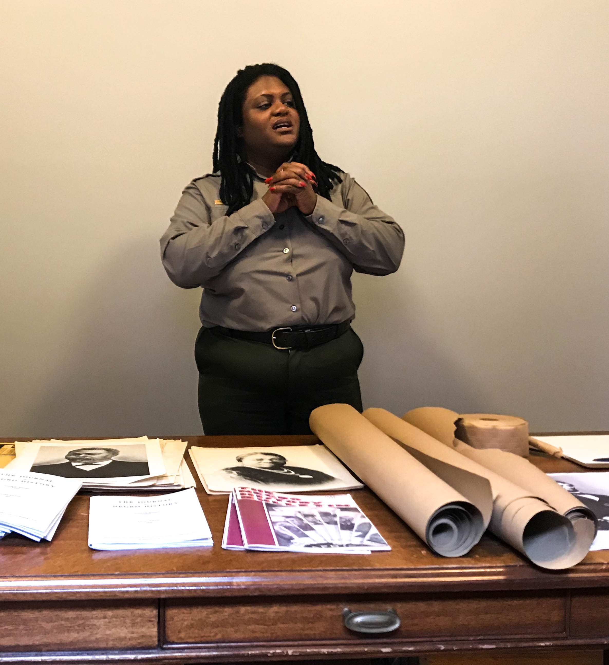 Ranger talking behind a table covered in papers that include images of Carter G. Woodson and Mary McLeod Bethune