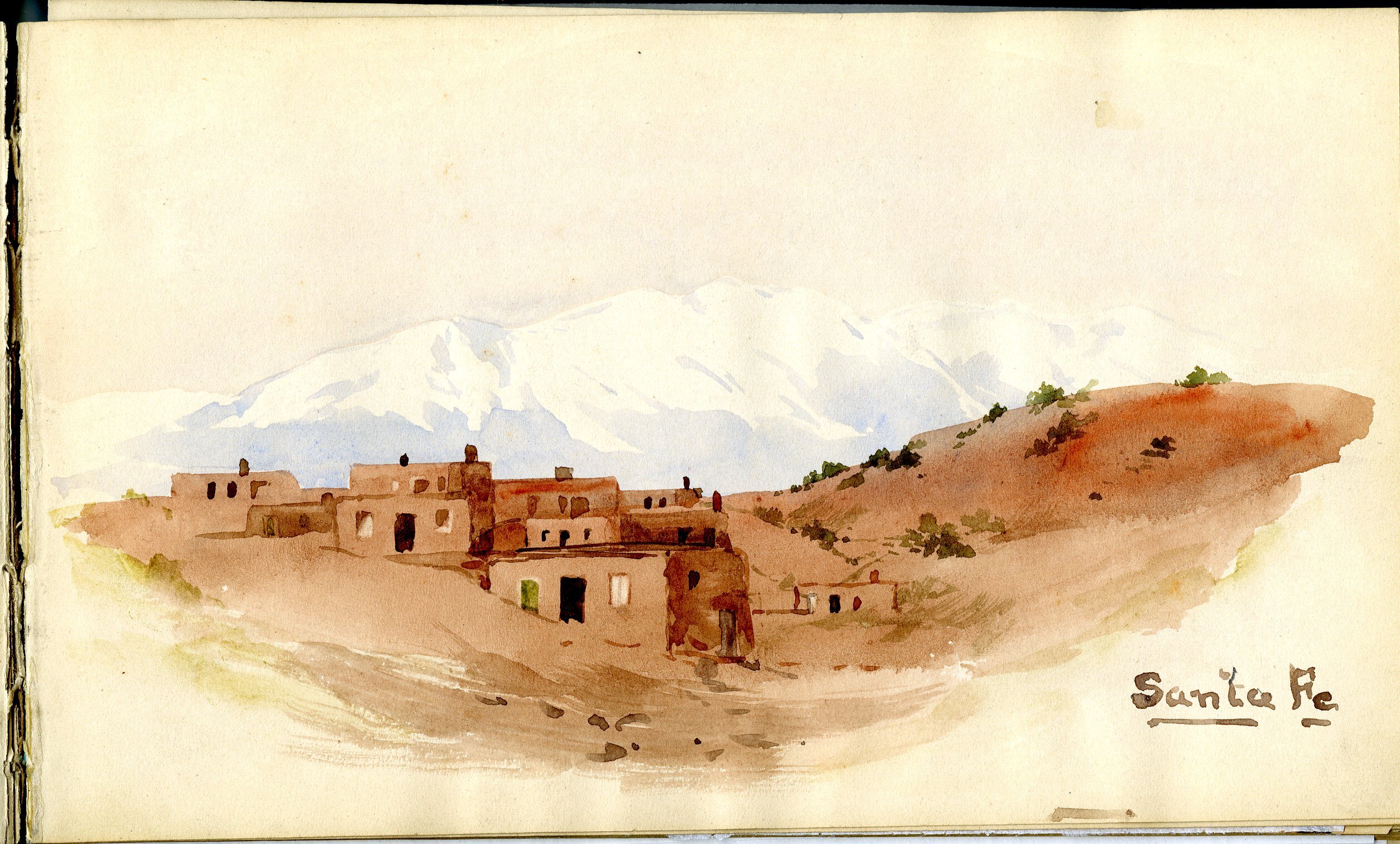 Landscape of Santa Fe with low adobe buildings on adobe-colored hills.  White mountain range in background.
