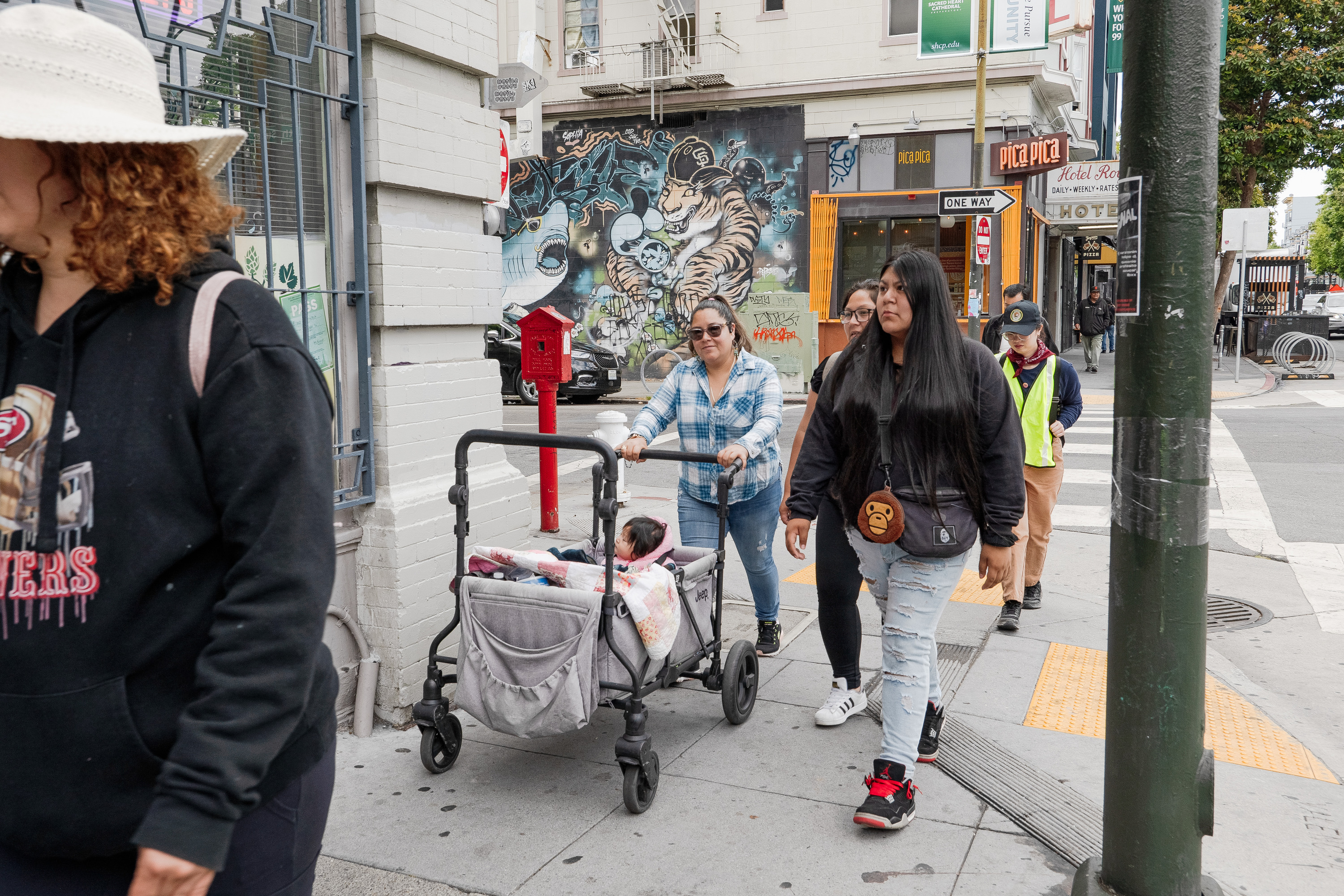 A group of women walk with a baby in a wagon across a city street