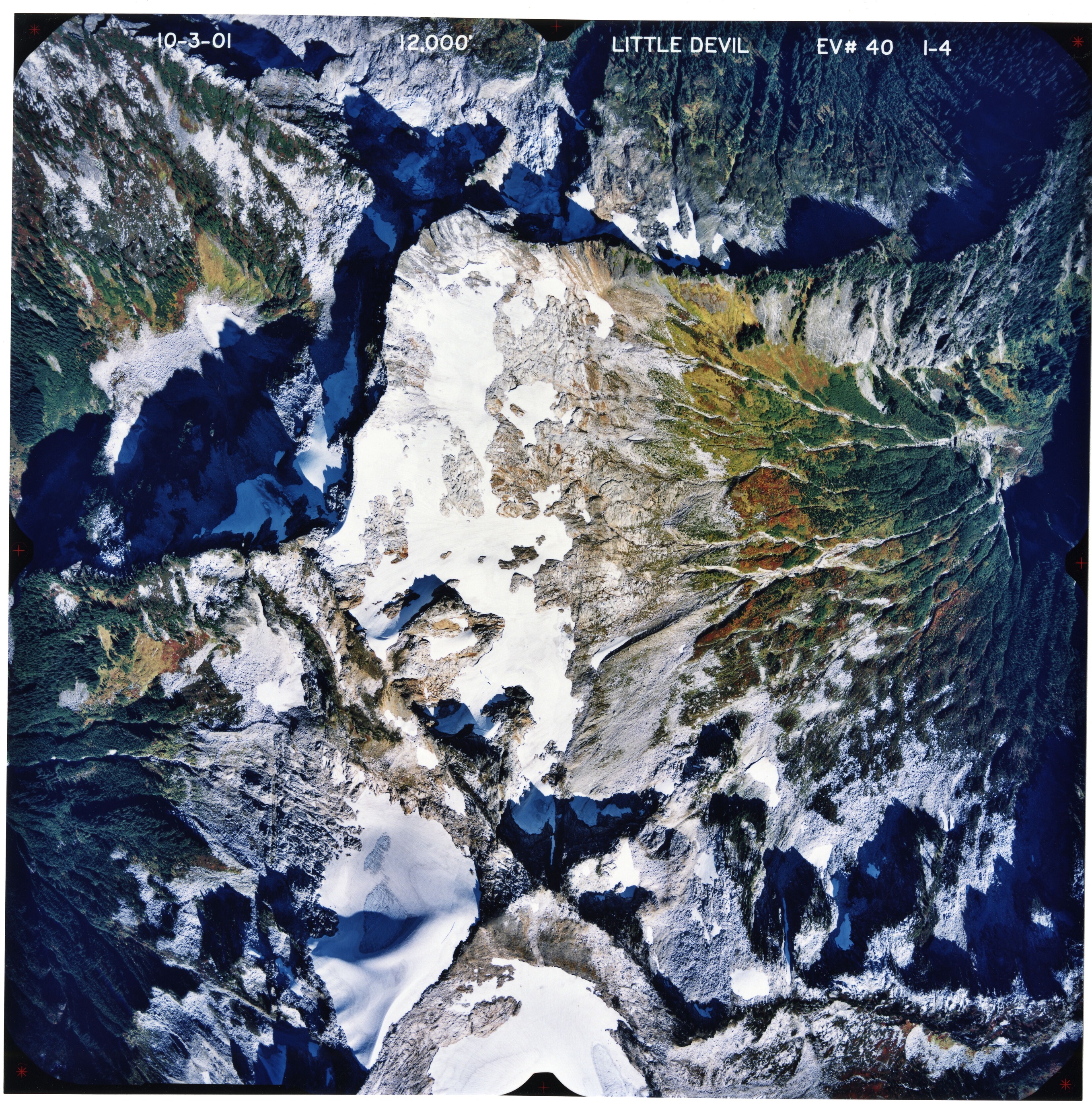 Color aerial photograph of glaciated mountain peak with forested valleys below.