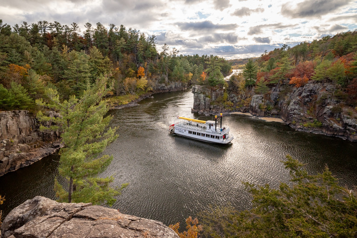 Photograph of river valley in autumn with large paddle-style river boat travelling across the water. 