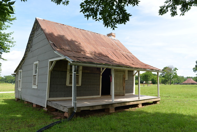 A raised cabin with a porch is surrounded by grass.