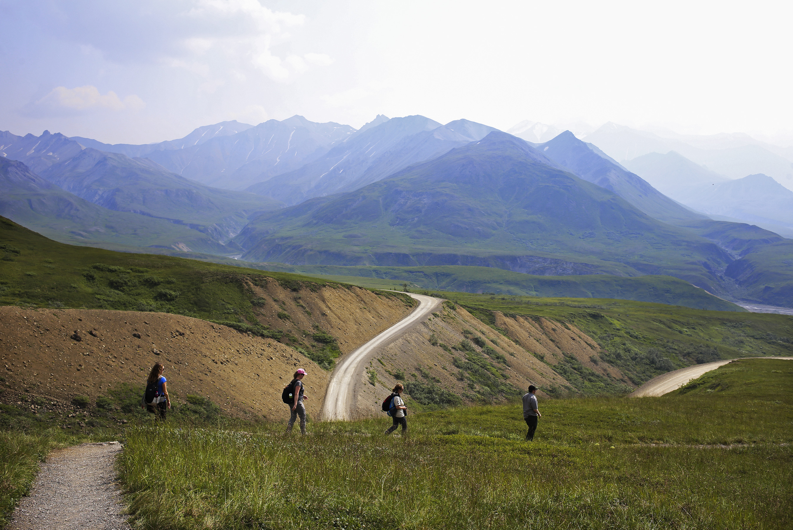 people hiking a trail on a tree-less mountainside