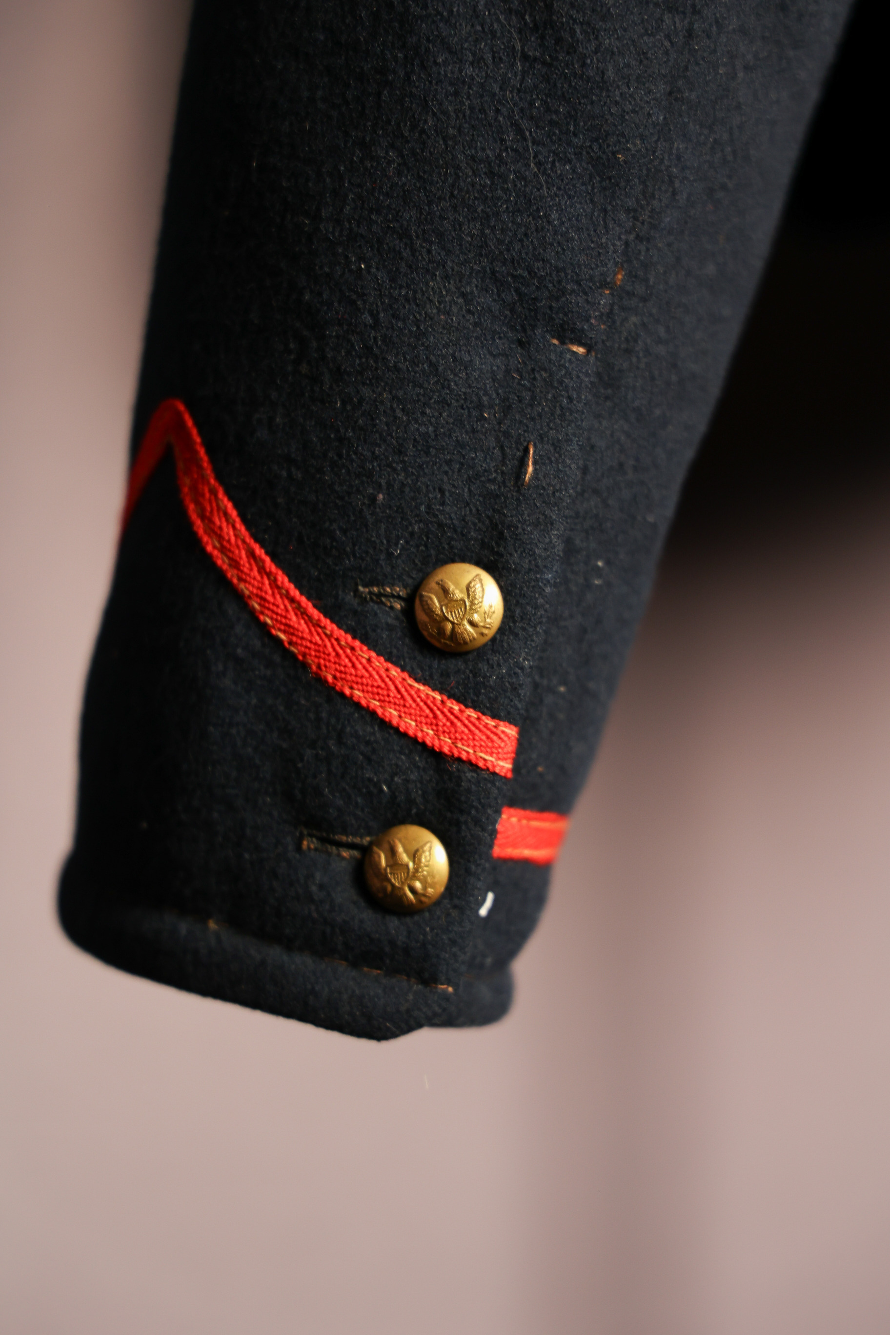 Color detail image of the field artilleryman shell jacket sleeve cuff. Image shows the orange piping and the two small, circular gold metal buttons. There is an eagle, wings spread, holding an olive branch and three arrows with a shield in the middle on each button.