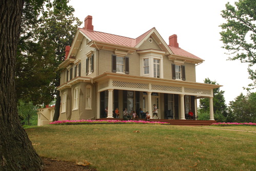 Several people sit on the porch of a large, two story house. 