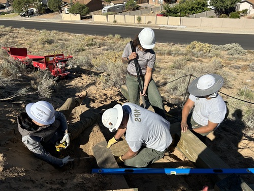 Four workers construct a trail with a road in the background.