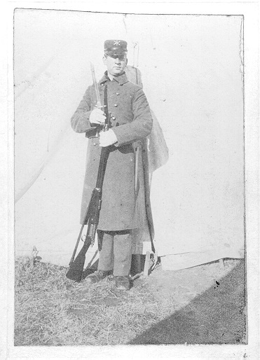 One many in Coast Artillery Uniform, winter gear, holding his rifle and bayonet.  Posing in front of a tent.