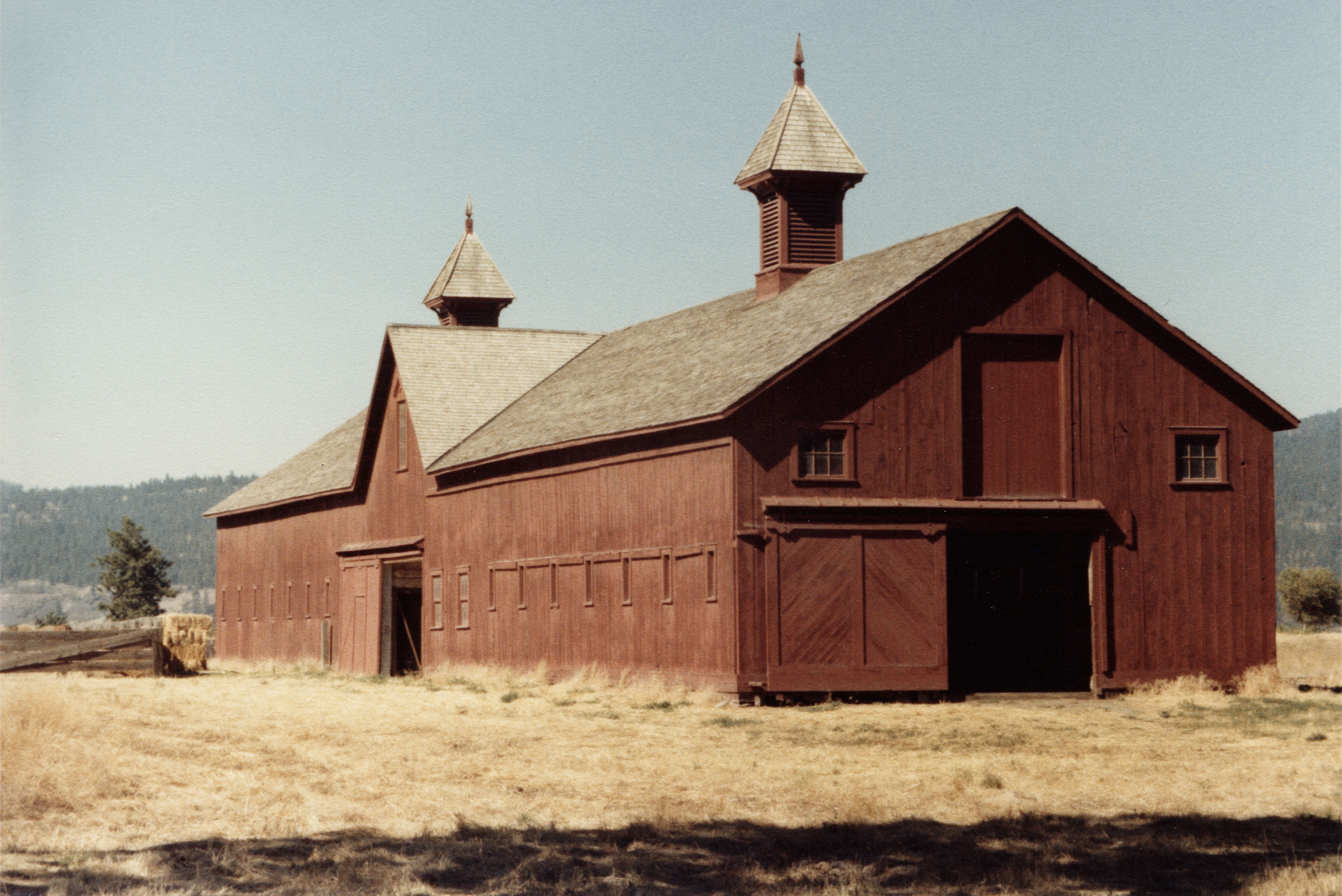 A color photograph of a red barn in a field. 