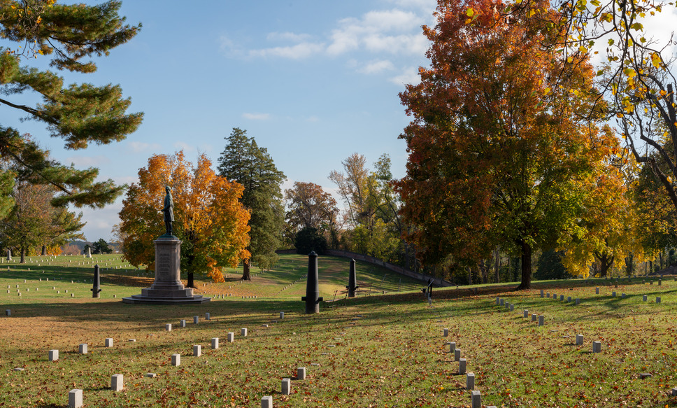 Landscape in a cemetery with a statue of Civil War general atop a stone base platform surrounded by yellow, green, and orange trees.