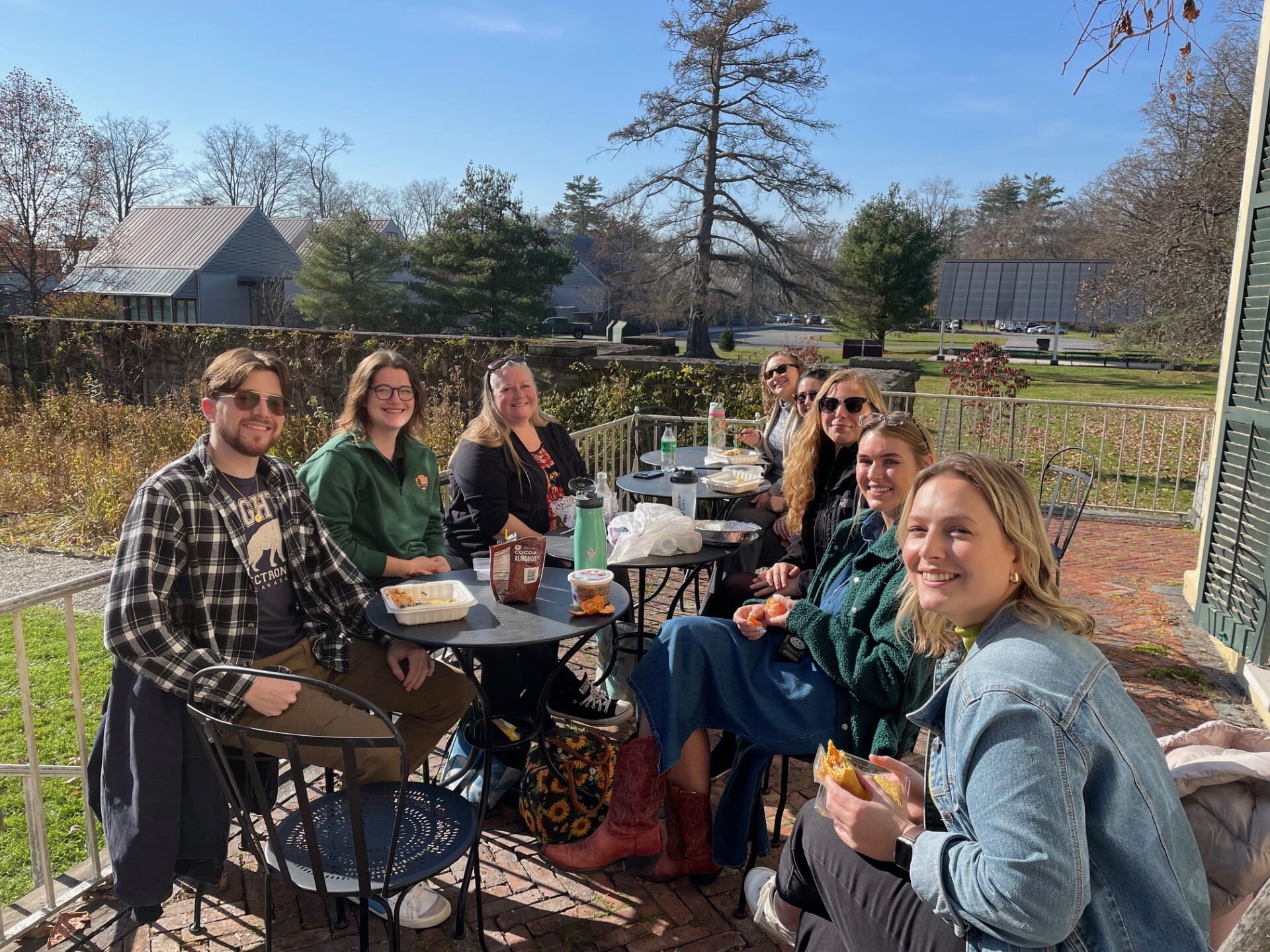 People gather outside eating lunch near a garden. 