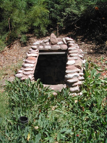 The dark entrance to a well is framed by stones with mortar on a slope.