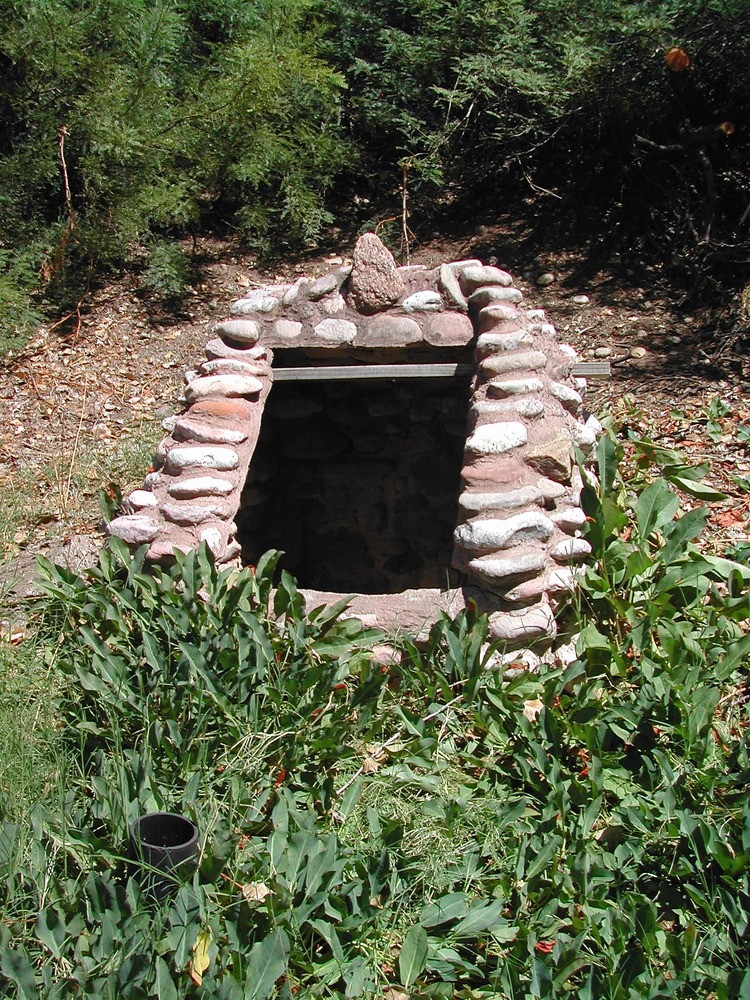 The dark entrance to a well is framed by stones with mortar on a slope.