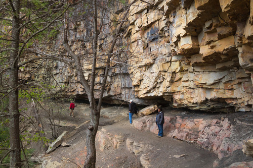 hikers on a trail at the base of a huge rock cliff