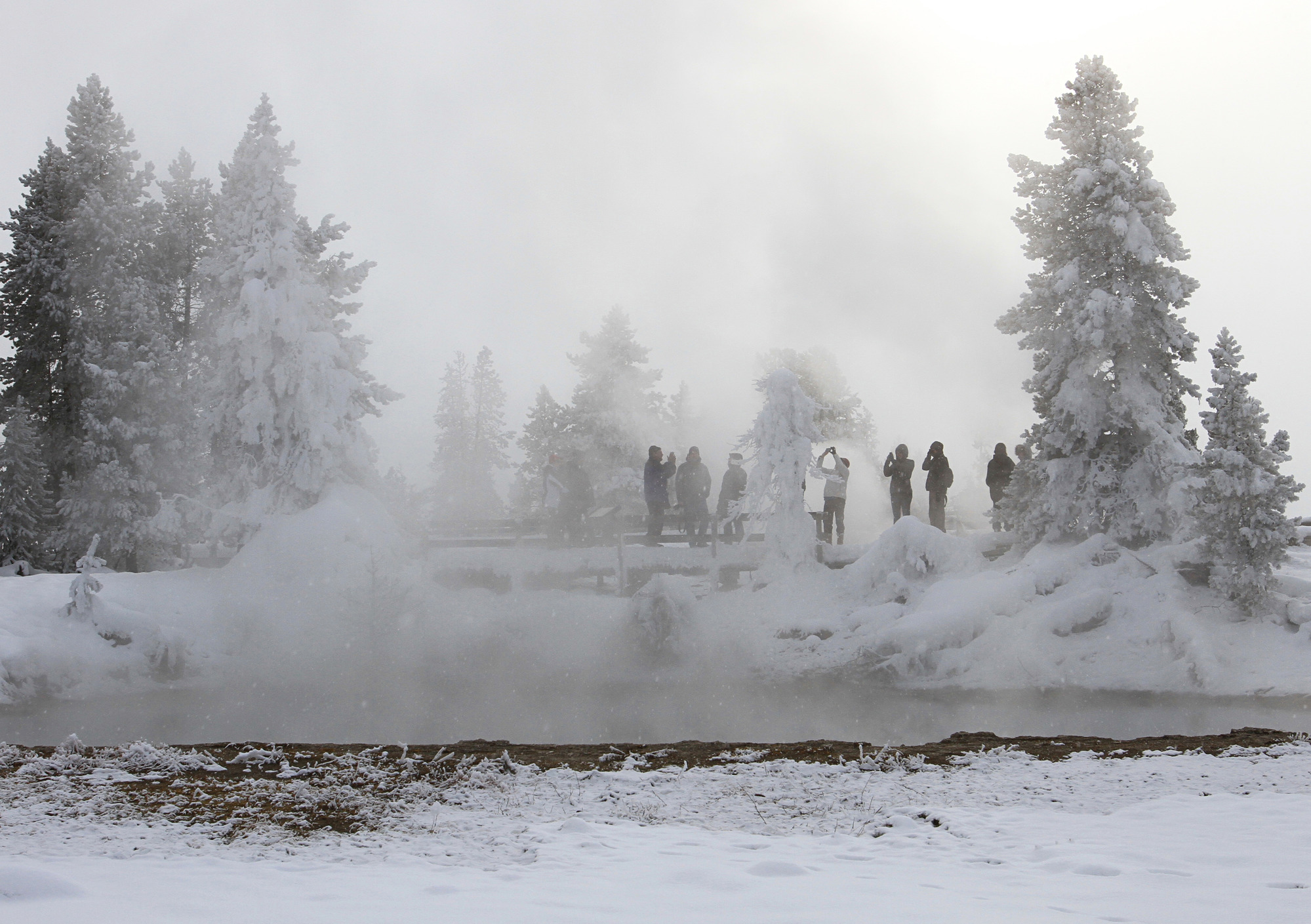 Visitors stand on boardwalk behind a steamy hot spring