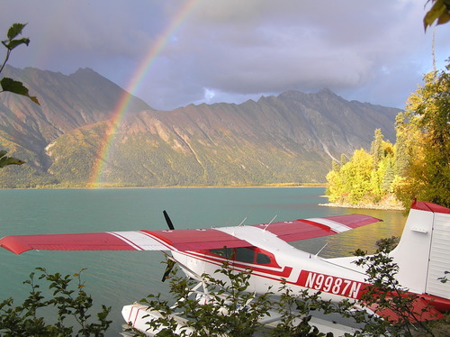 A red and white airplane on a lake across from a rainbow and mountains