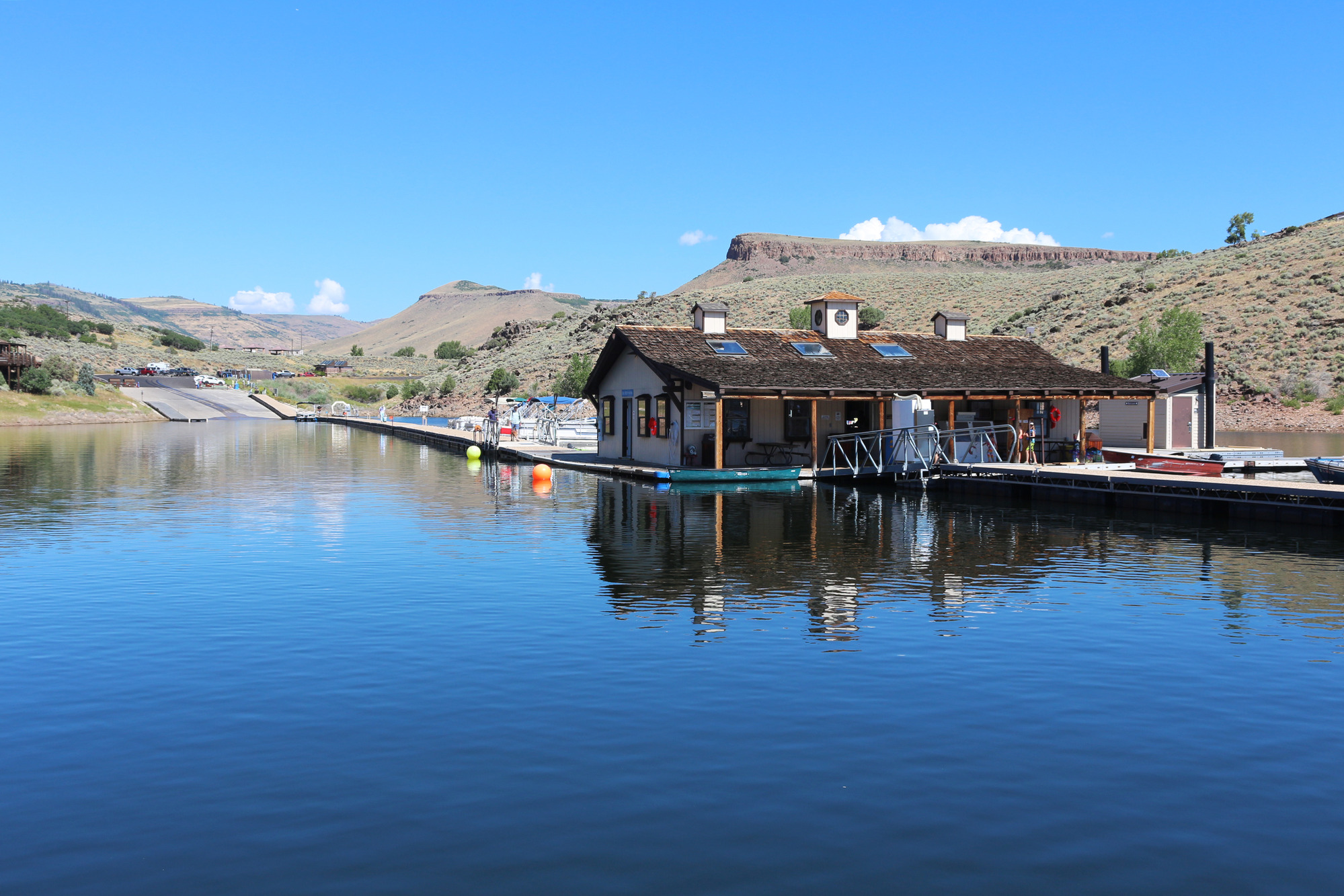A white building with a brown roof stands on a floating dock. A large ramp is in the background with a long walkway leading to the building.