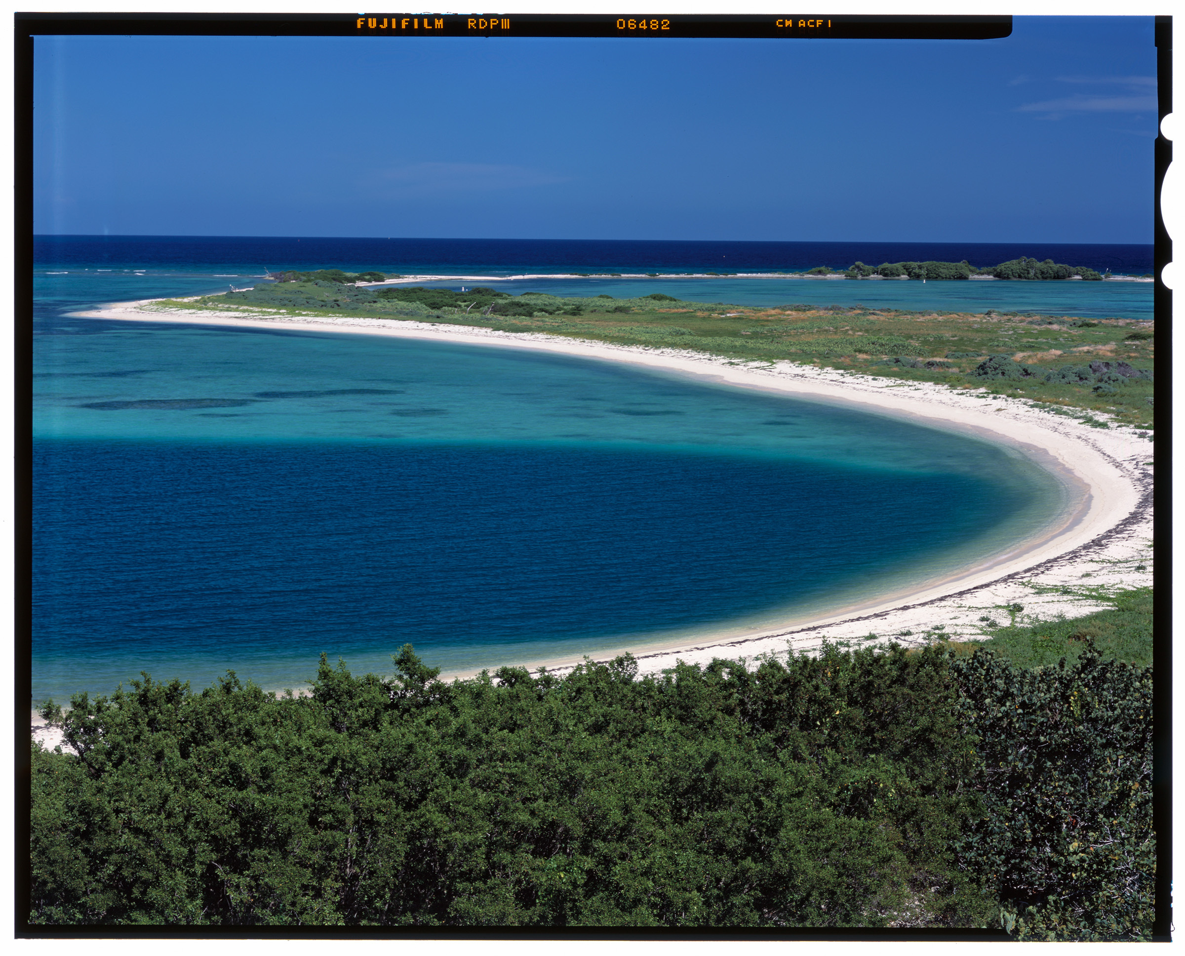 View of curving white beach and greenery with blue-green water