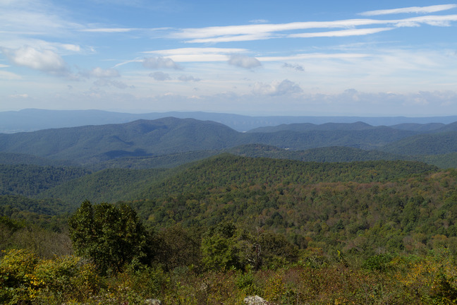 Several mountain ranges that are a mixture of green and brown in the foreground transitioning into blue in the background. 