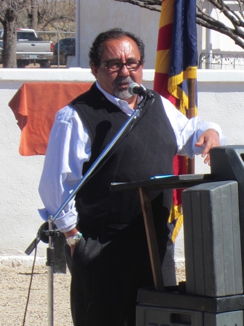 A person with short hair, a goatee, and glasses speaks into a microphone