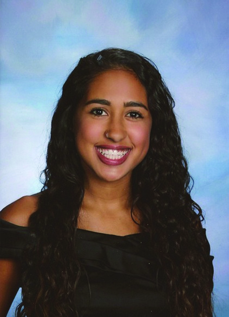 A professional headshot of a woman with curly dark hair and bright smile.