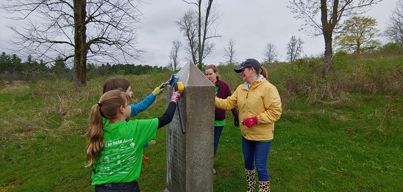 Four volunteers, including two children, scrub a monument with plastic brushes