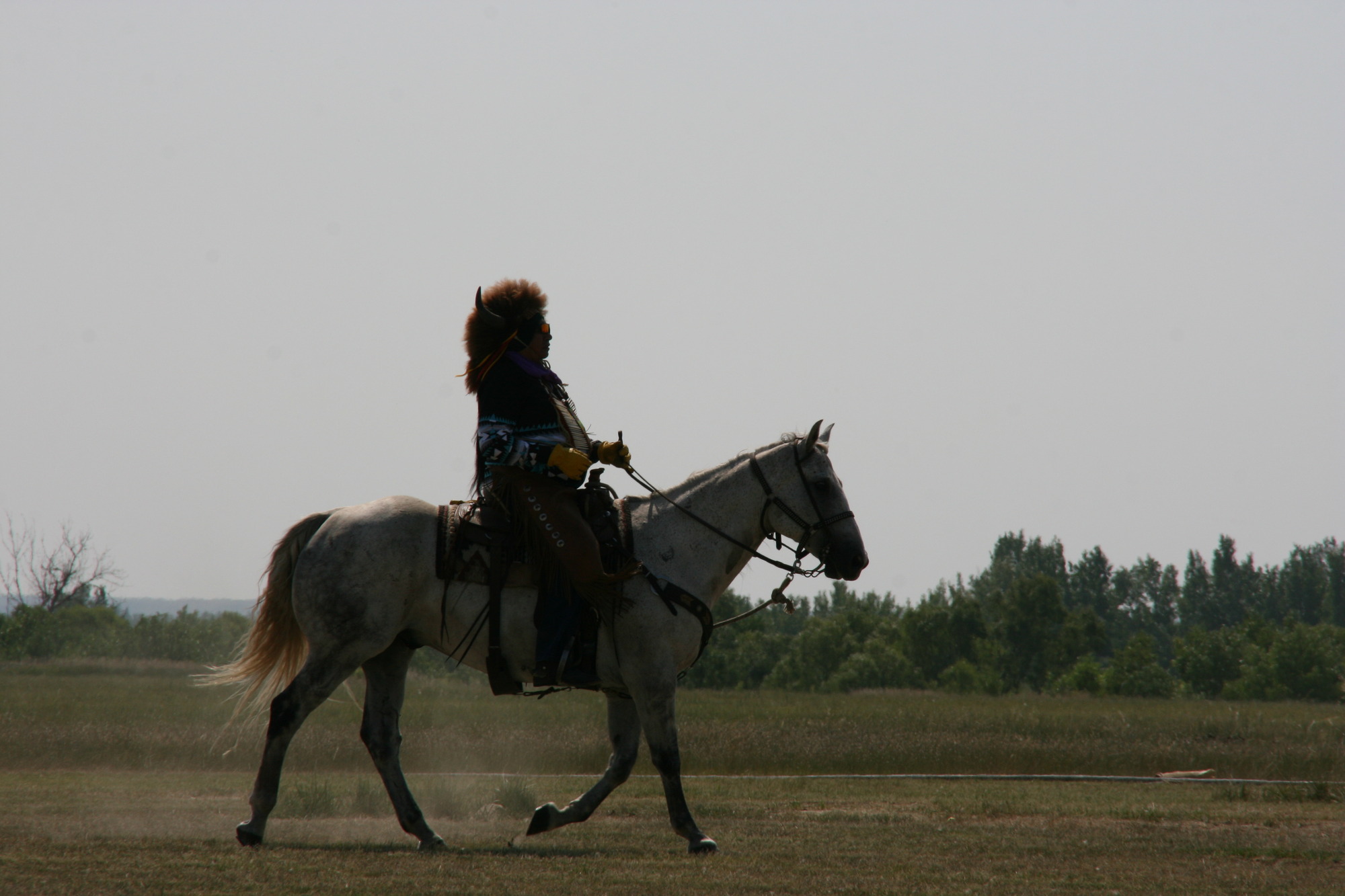 Man on horseback wearing traditional American Indian dress including a large fur hat with horns.