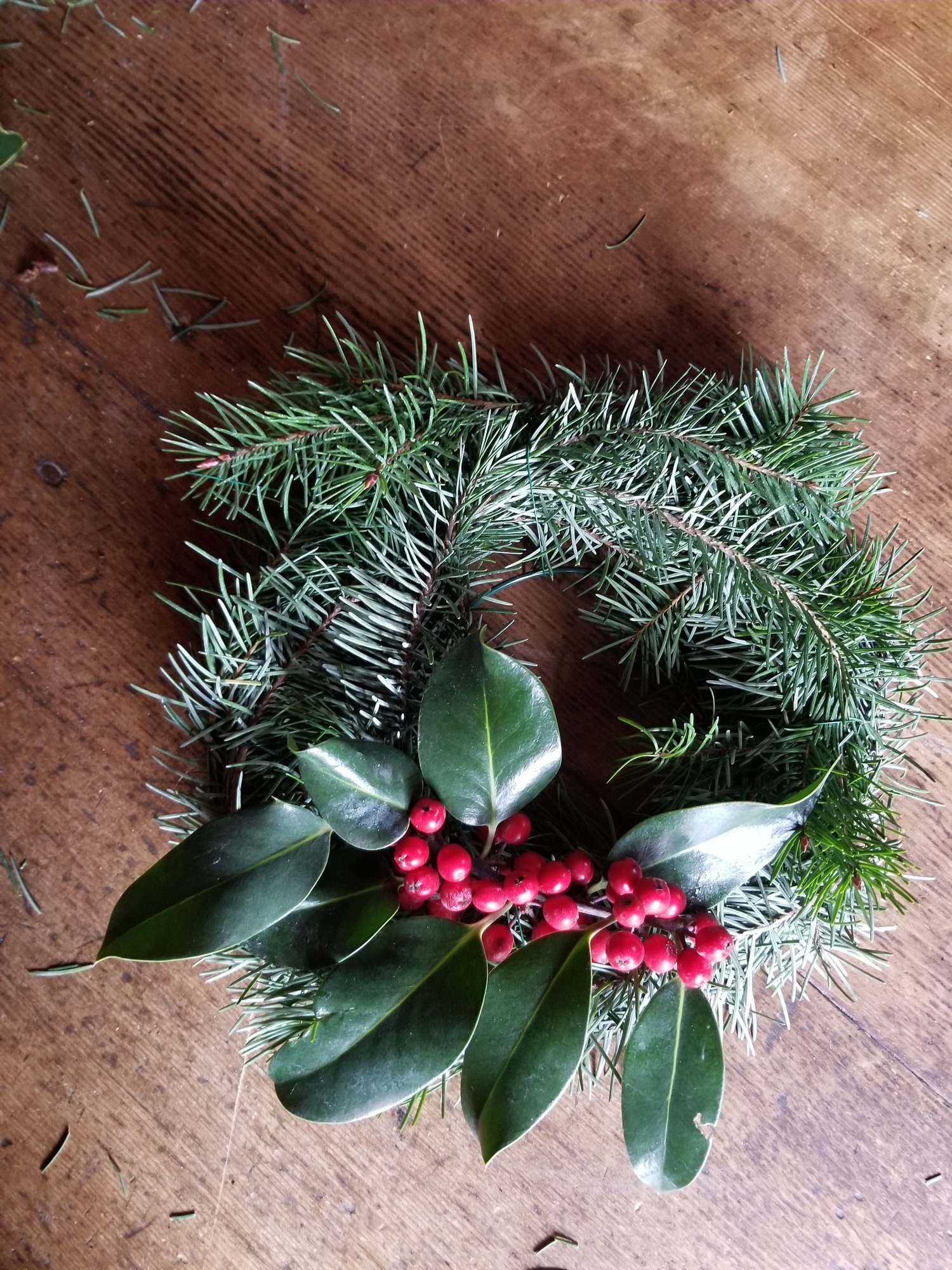 The wire wreath frame with evergreen boughs attached and a sprig of holly with red berries.