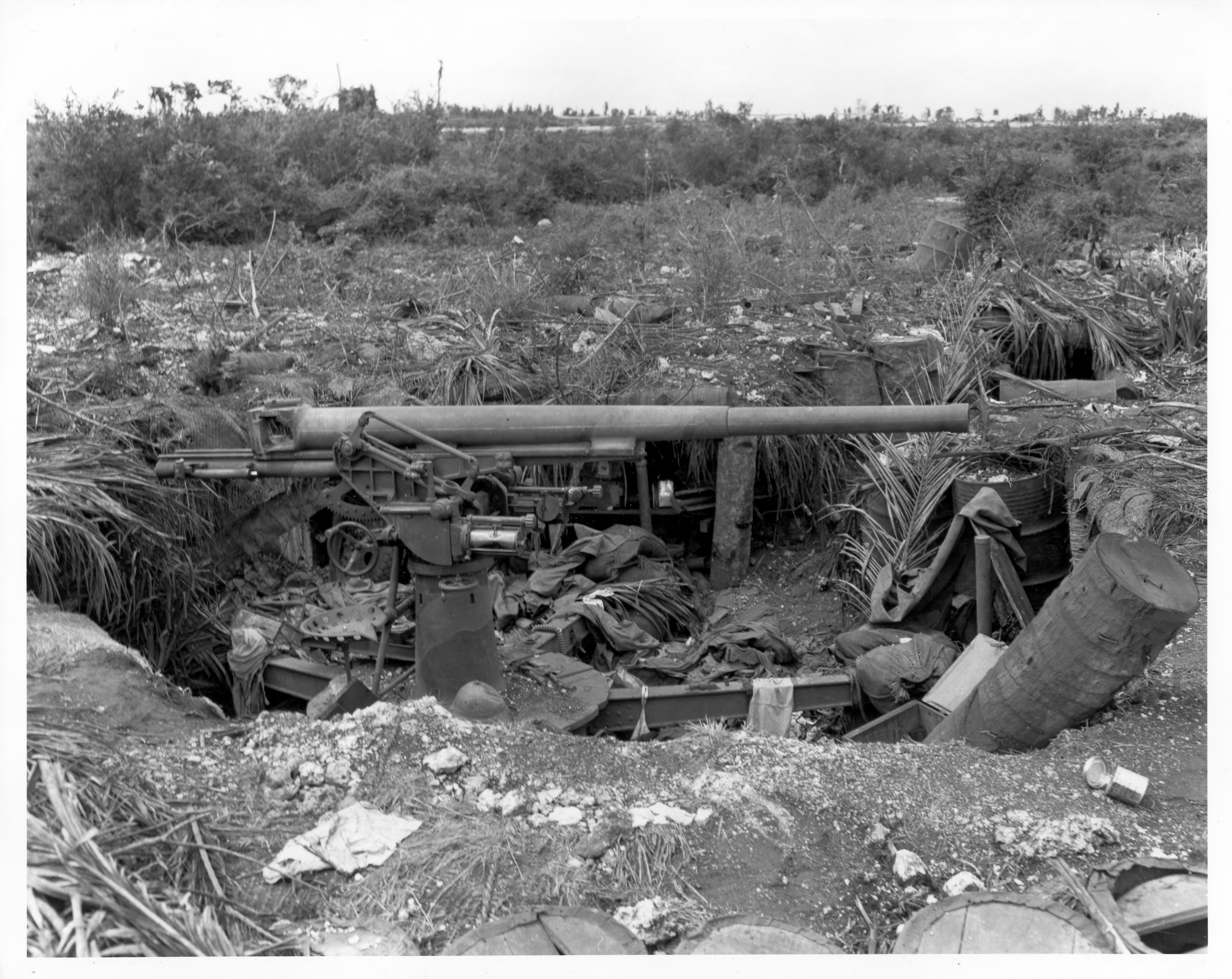 Black and white photo of a large gun in a dug out surrounded by rubble.