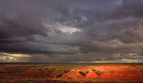 Dark monsoon clouds over sun highlighted red badlands