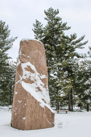 Granite monolith on a plaza surrounded by trees after a snowfall