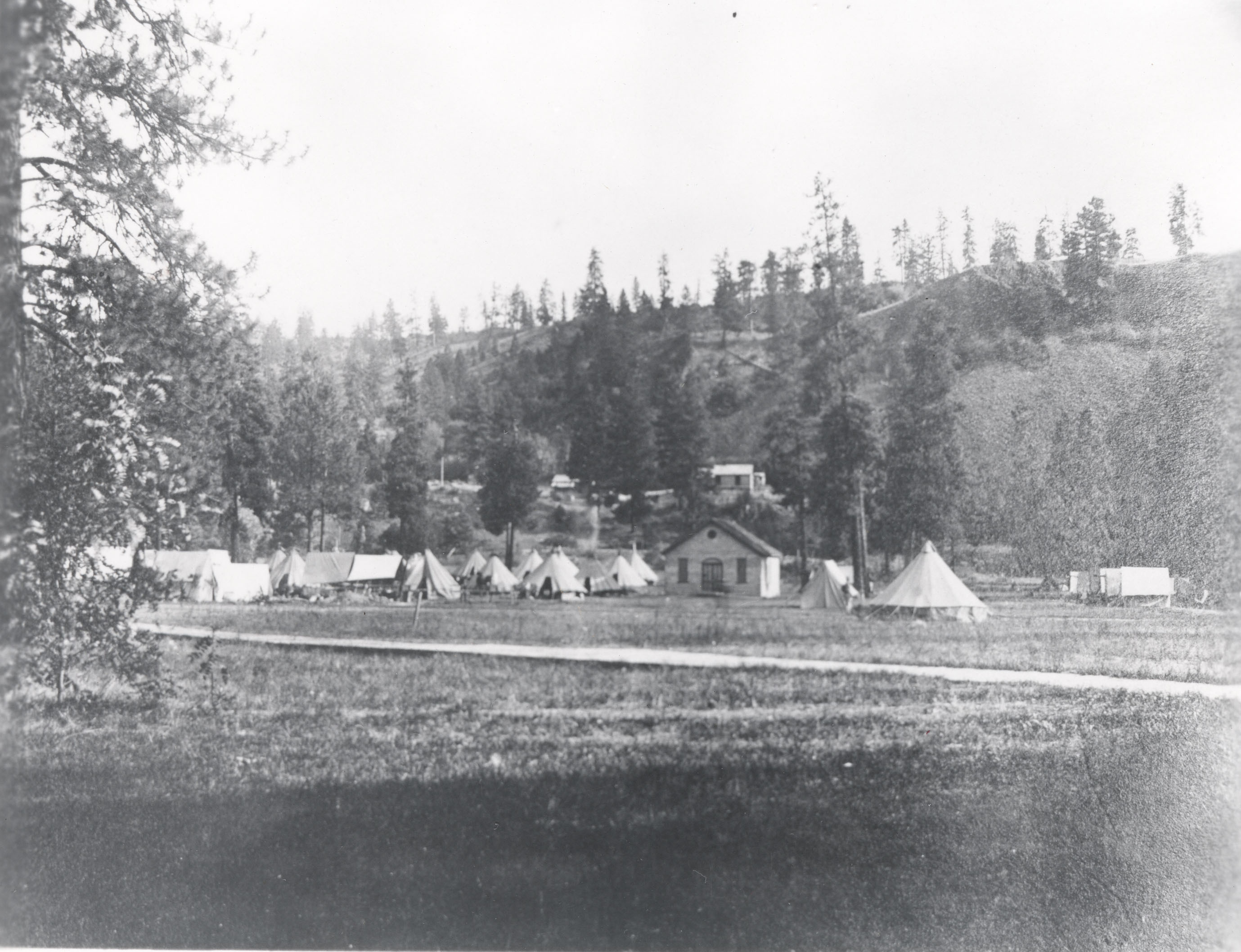 Black and white photograph of tents and buildings in a field